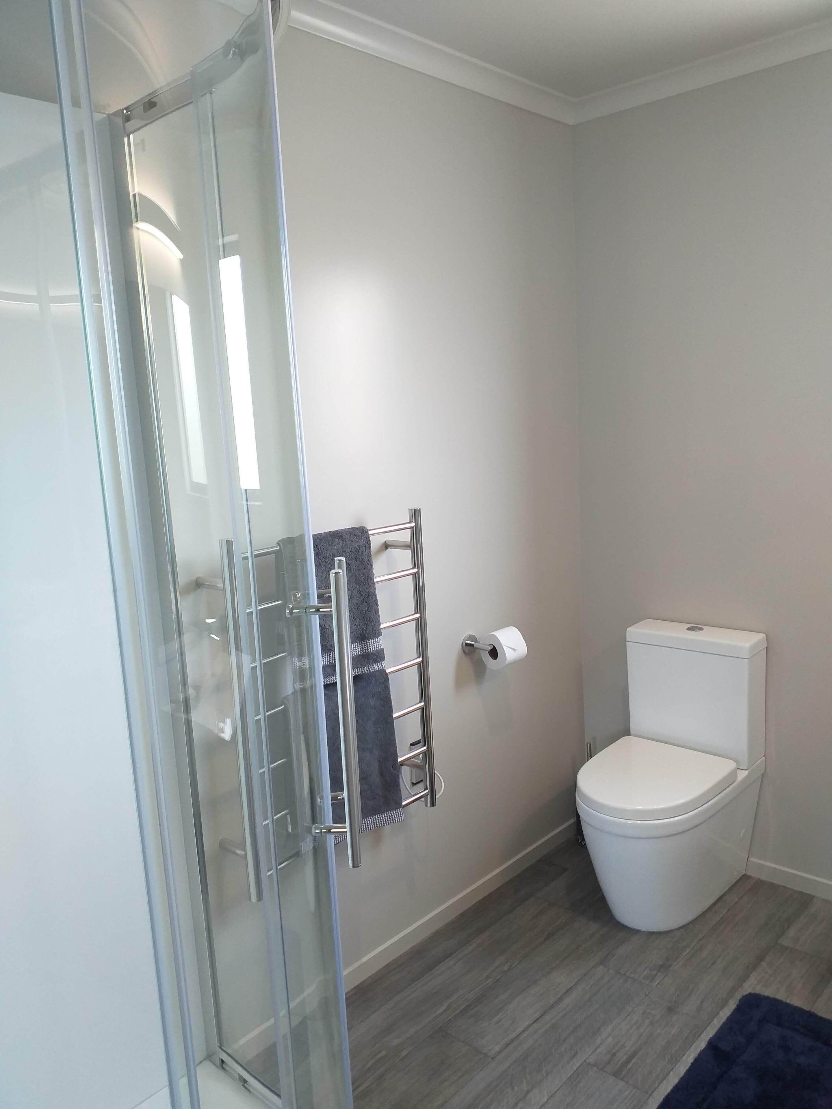 A bathroom with a glass shower enclosure, a towel rack with a towel, a toilet, and a dark blue rug on the floor.