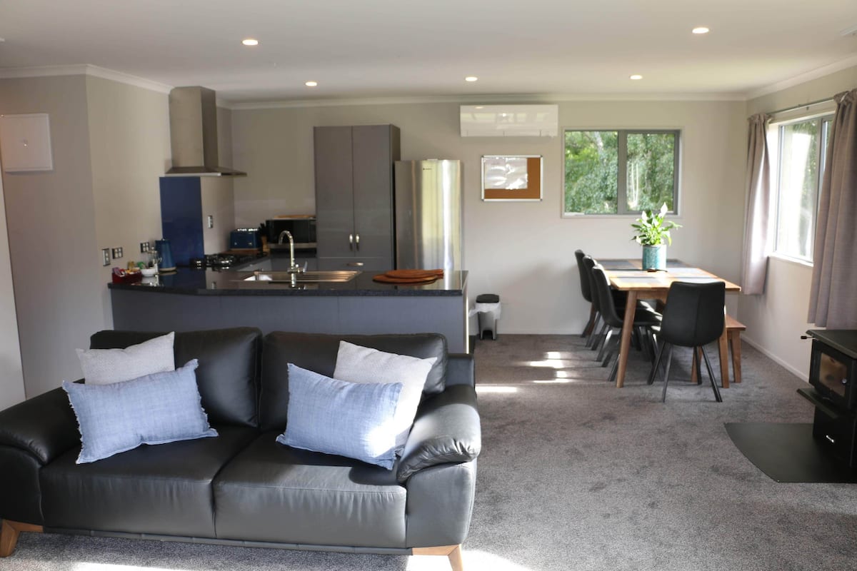 A modern living room with a sofa, a dining area with a table and chairs, and a kitchen with a stove and cabinets.