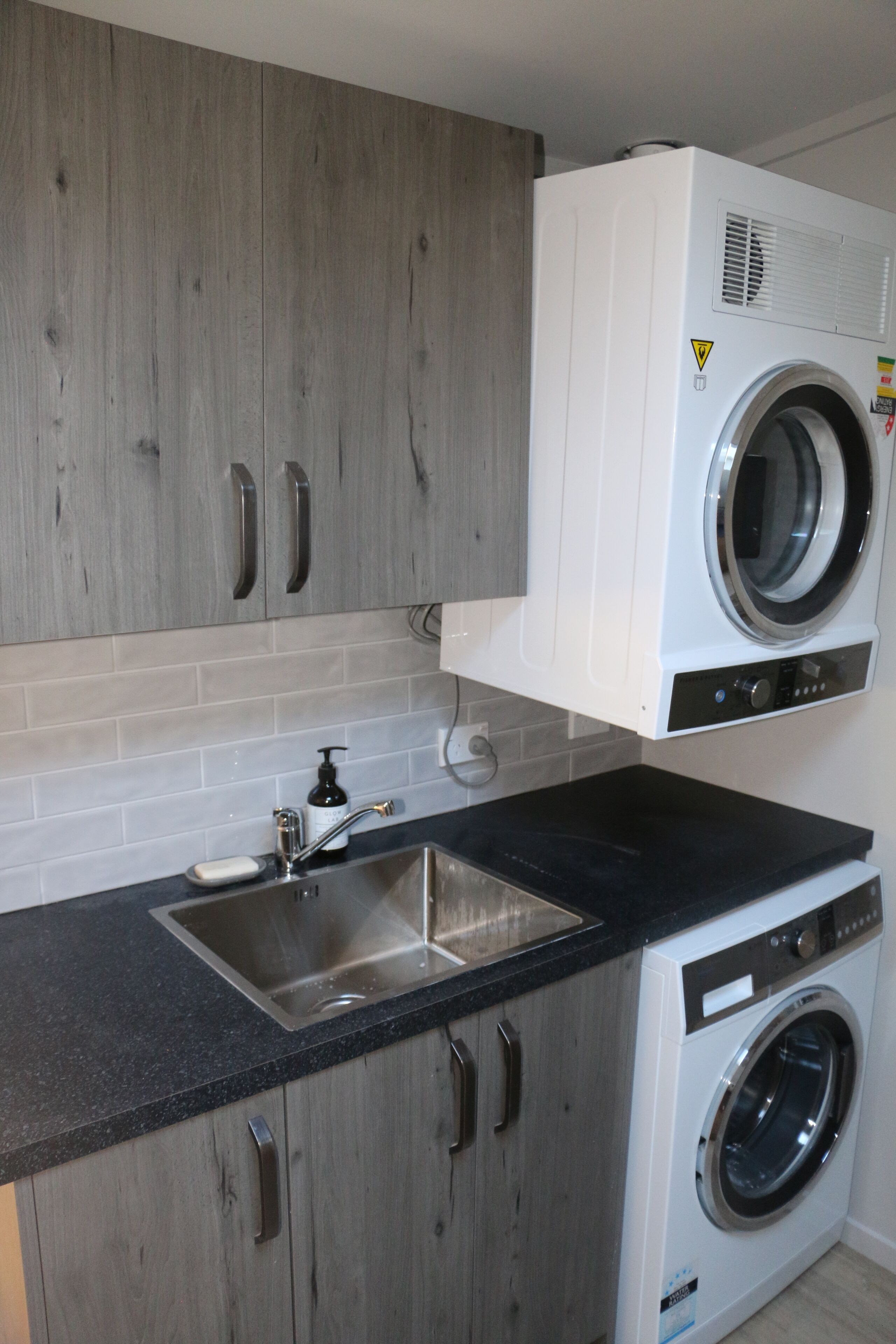 A compact kitchen with grey cabinets, a black countertop, a stainless steel sink, and a built-in washing machine.