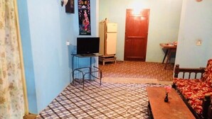 A small, compact living space with a patterned floor, a sofa, a TV, and a refrigerator. - Mahagedara Home Stay (Laggala-Pallegama)