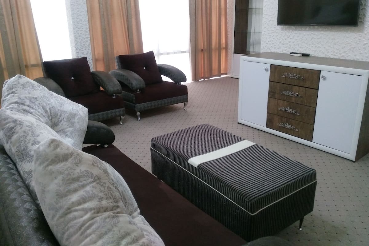 A modern living room with a sofa, armchairs, a TV, and a cabinet.