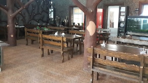 Un restaurant amb taules i bancs de fusta, una gran escultura d'arbre i una paret de pedra.