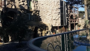 Zona de piscina amb un mur de pedra i un edifici modern amb teulada verda.