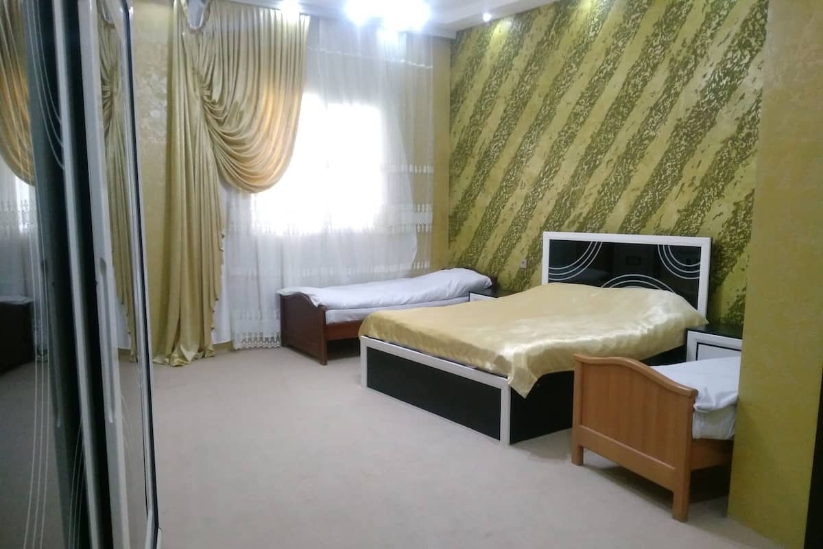 A bedroom with two single beds, a large window with sheer curtains, and a patterned wall.
