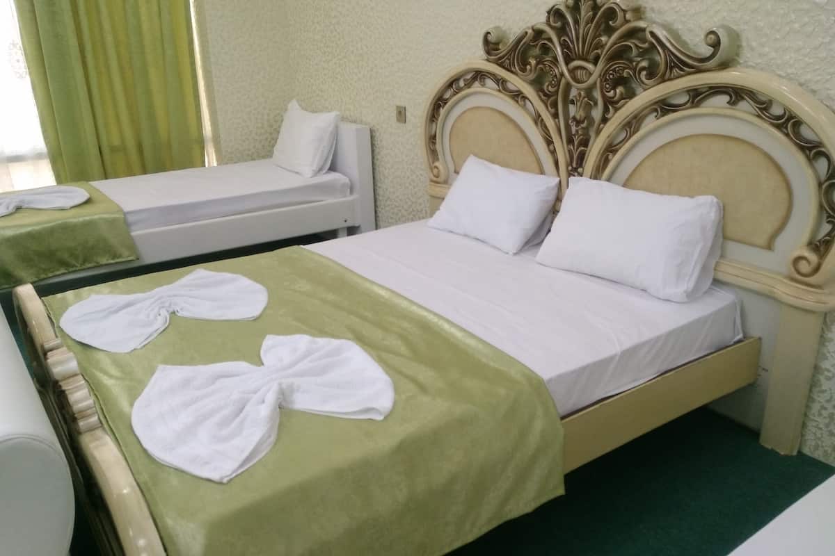 A hotel room with two beds, each with a green bedspread and white linens.