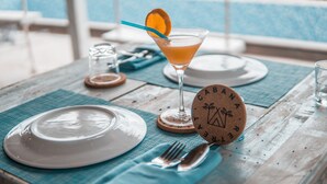 A table set with plates, cutlery, a cocktail glass with an orange garnish, and a wooden coaster with a tent design.