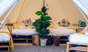 A cozy tent with two beds, each with a pillow and a small table. There is a large plant in the center. - Cabana Retreat - Glamping (Kota Belud)