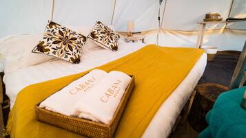 A bed with a yellow blanket, two patterned pillows, and a basket with a towel labeled "CABANA RETREAT".