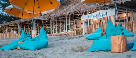 A beachside restaurant with thatched roofs and string lights.