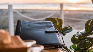 A black leather wallet with "CABANA RETREAT" embossed on it, placed on a table with a plant beside it.