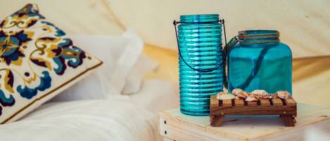 A wooden nightstand with a teal glass jar and a smaller jar, a wooden crate with seashells, and a decorative pillow with a floral pattern.