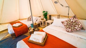 A tented accommodation with two beds, a small table, a lamp, and a plant.