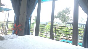 A room with a bed, a fan, and large windows with curtains.