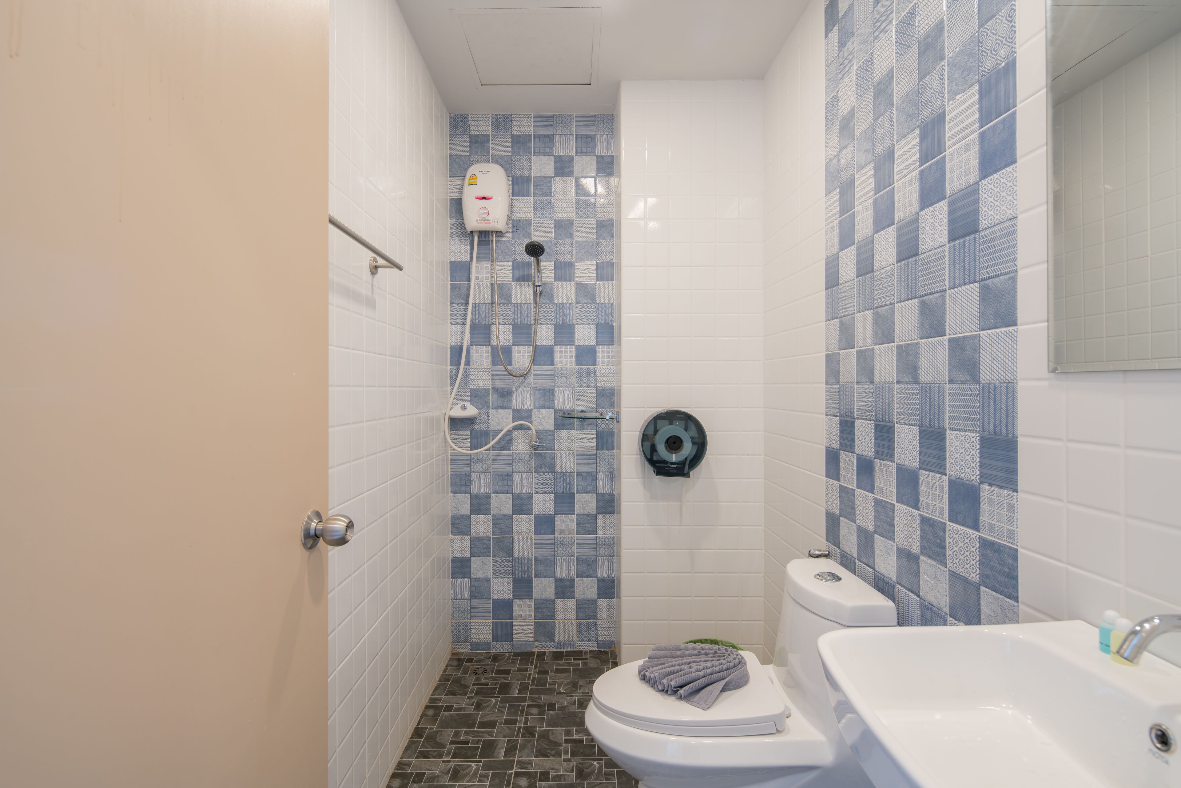 A bathroom with a checkered tile wall, a toilet, a shower with a handheld showerhead, and a sink.