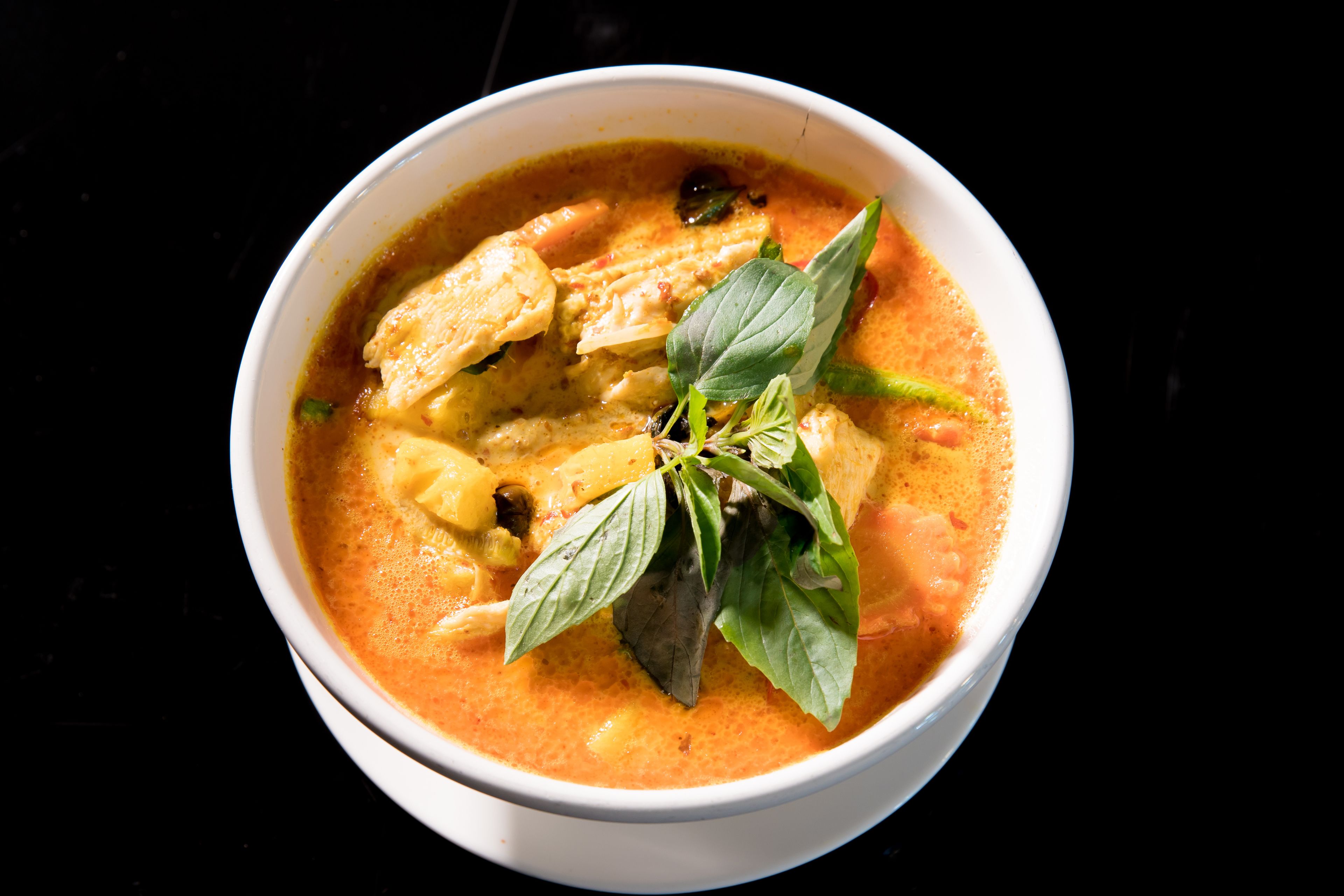 A bowl of soup with visible ingredients like chicken, herbs, and possibly vegetables in a creamy broth.