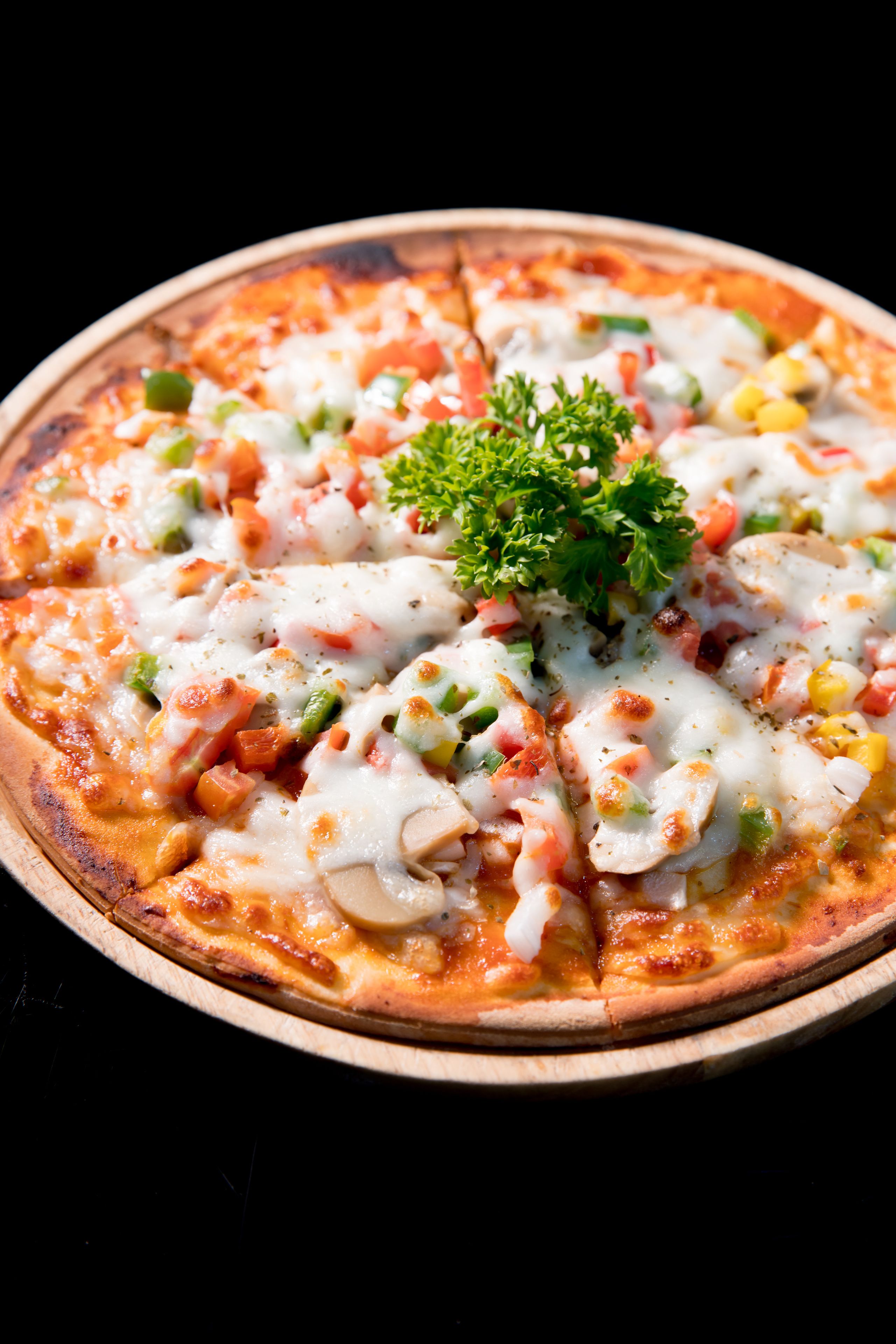 A pizza with various toppings and a garnish on a wooden plate.