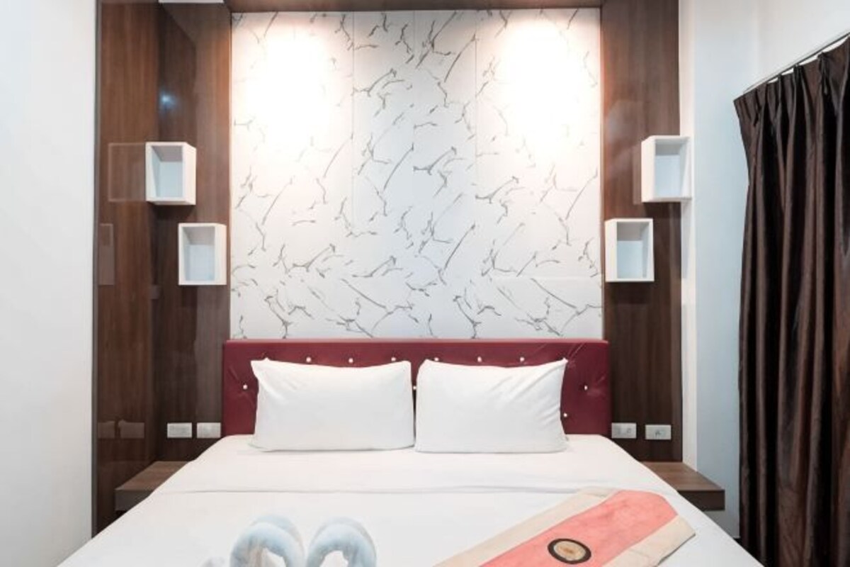 Habitación de hotel con cama, dos mesitas de noche, cabecera y pared con diseño de mármol.