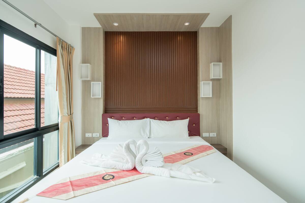Habitación de hotel con una cama grande, pared de paneles de madera y una ventana con cortinas.