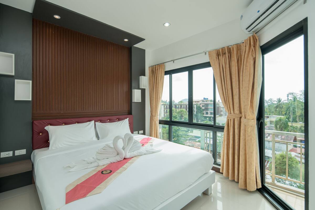 Habitación de hotel moderna con una cama grande, cabecera de madera y vistas a la ciudad a través de amplias ventanas.