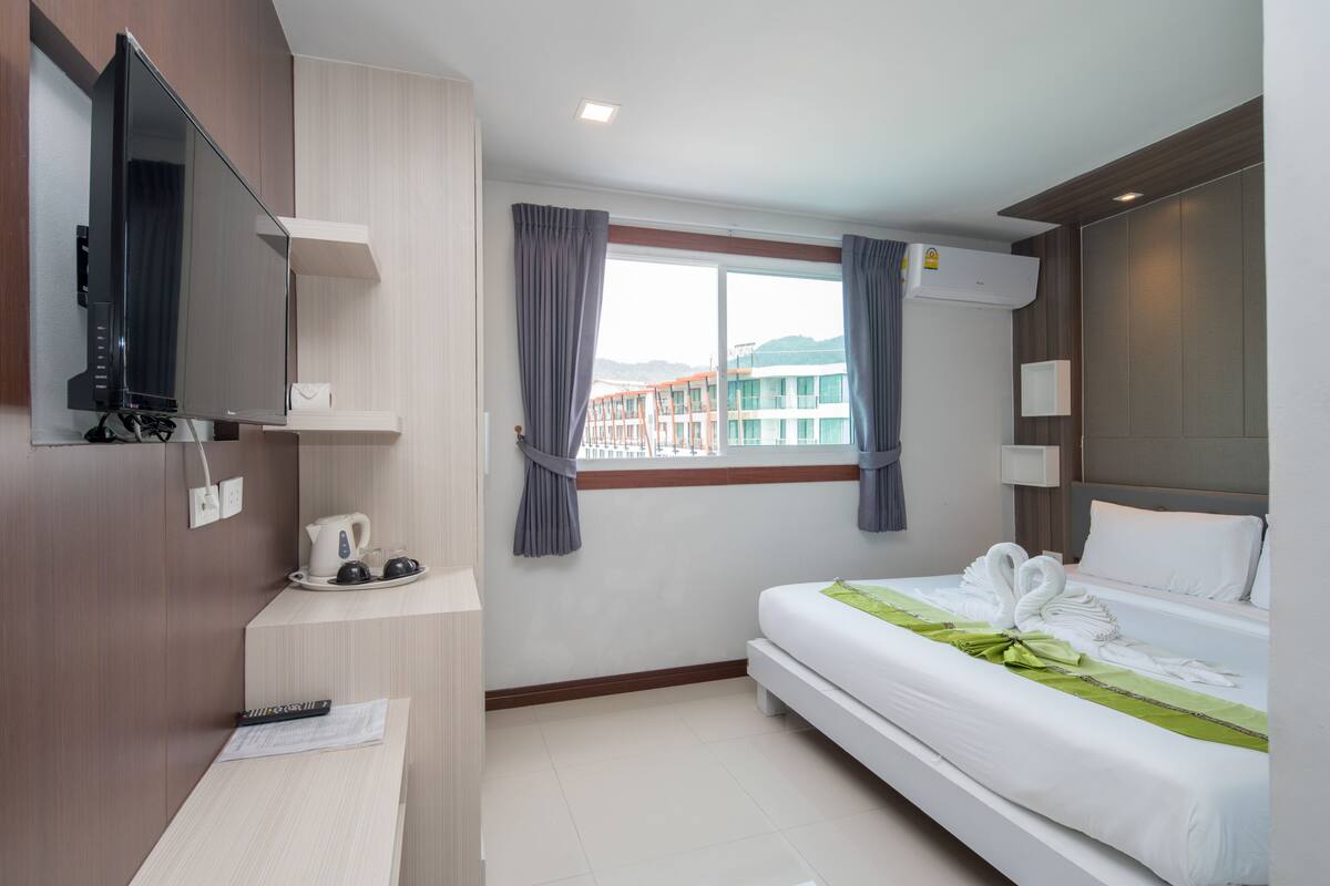 Habitación de hotel con cama, escritorio con hervidor, televisor de pantalla plana y ventana con cortinas.