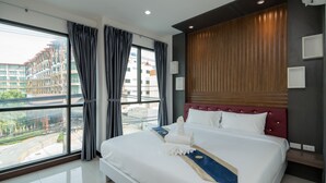 Quarto de hotel moderno com uma cama grande, cabeceira de madeira e vista para a cidade através de janelas do chão ao teto.