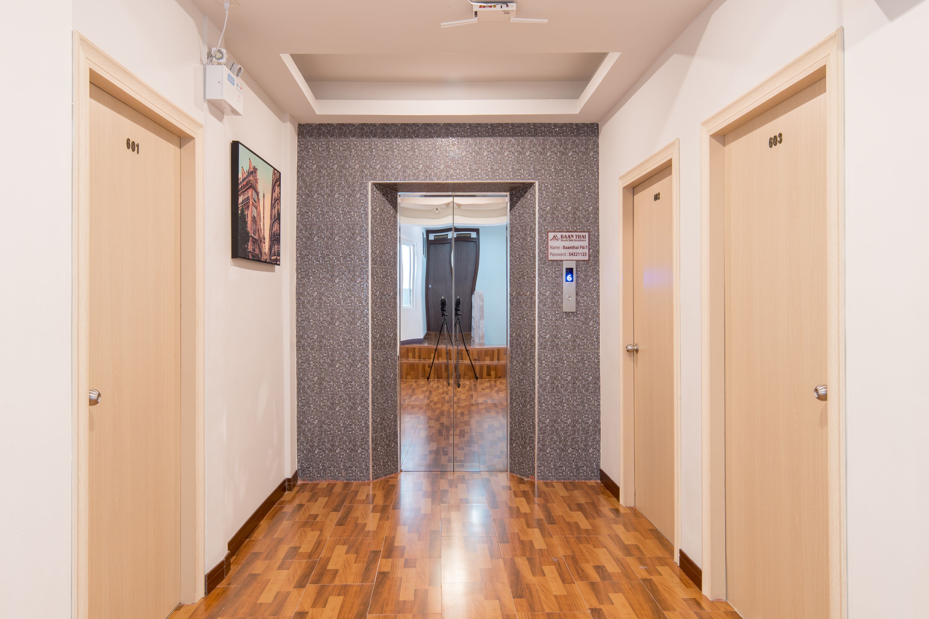 A hallway with wooden flooring, two doors labeled 601 and 603, and a sign indicating the name 'Baan Thai' with a nameplate and password.