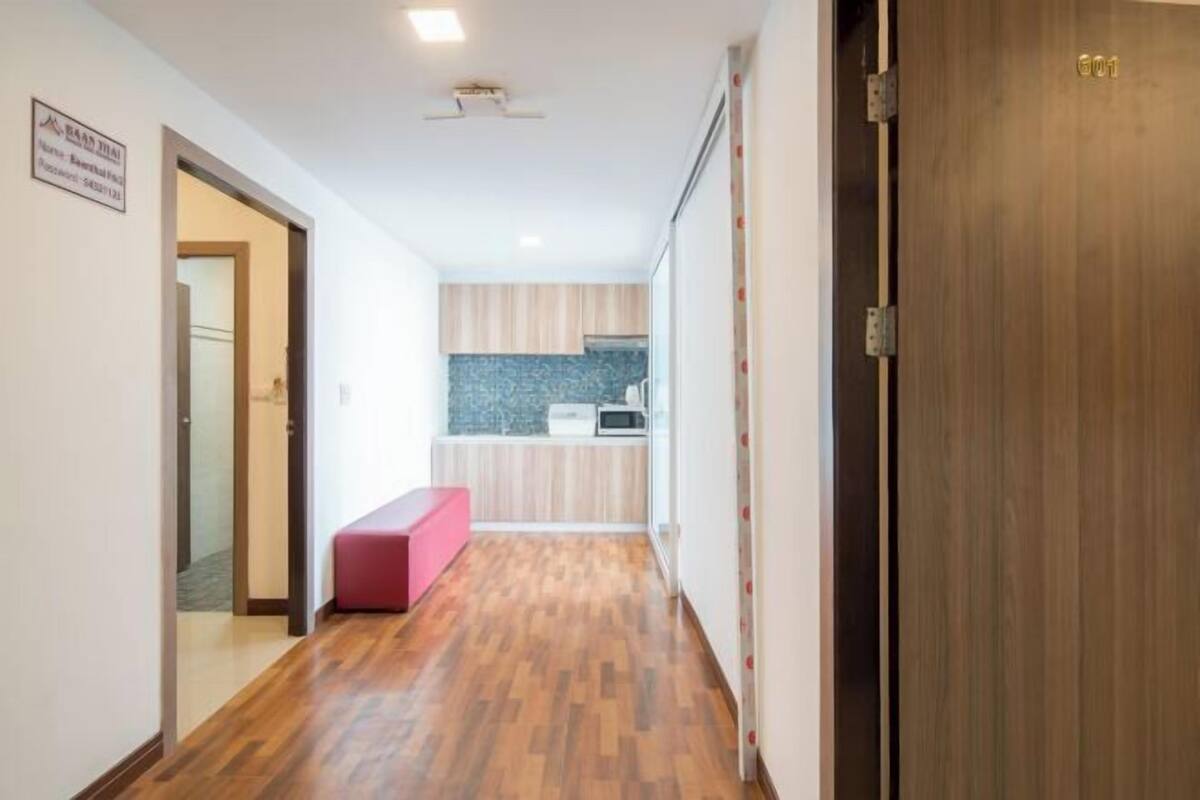 Un pasillo con suelo de madera, un banco rojo y una zona de cocina con armarios de madera y un microondas.
