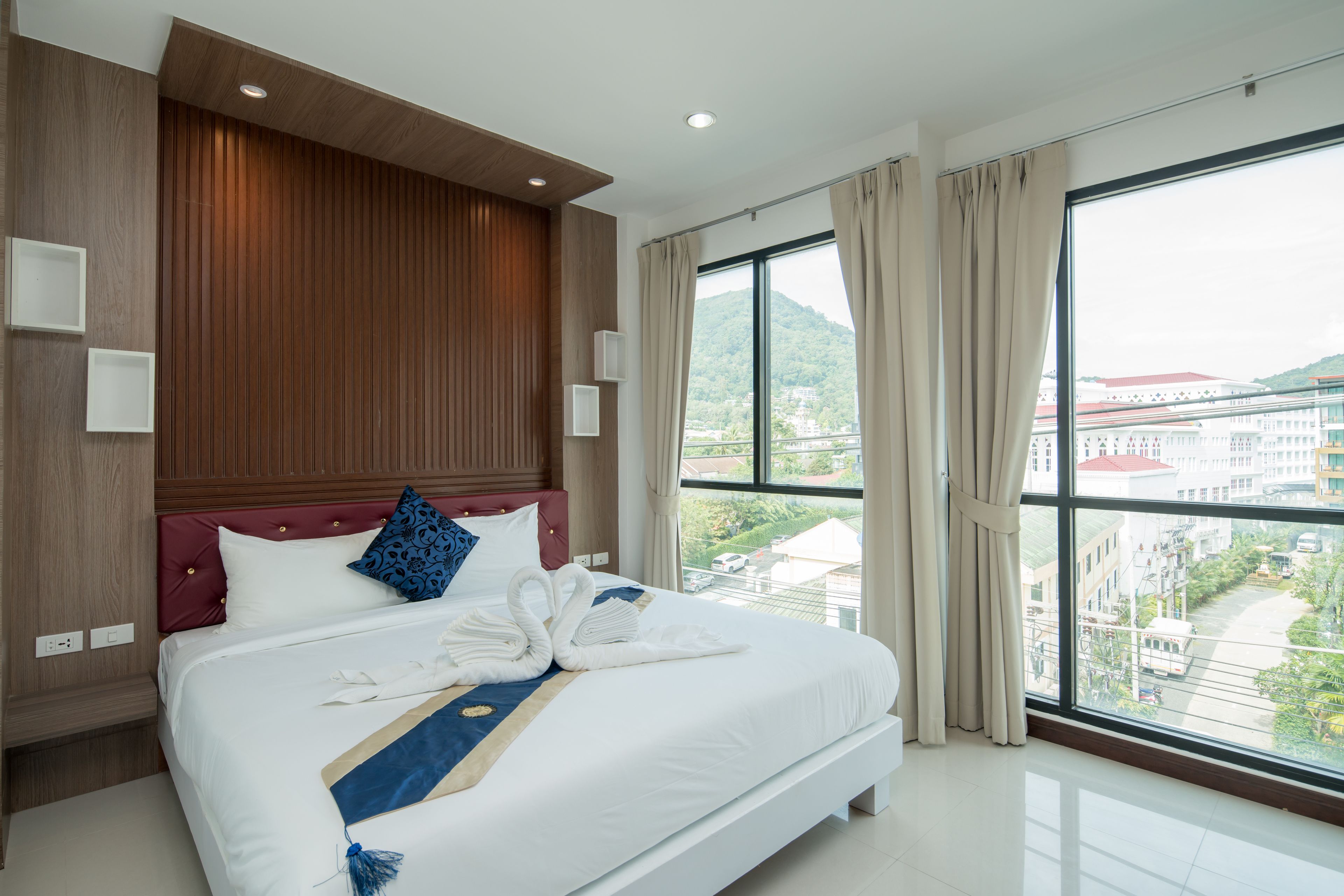 A modern hotel room with a large bed, wooden paneling, a view of the city, and a balcony.