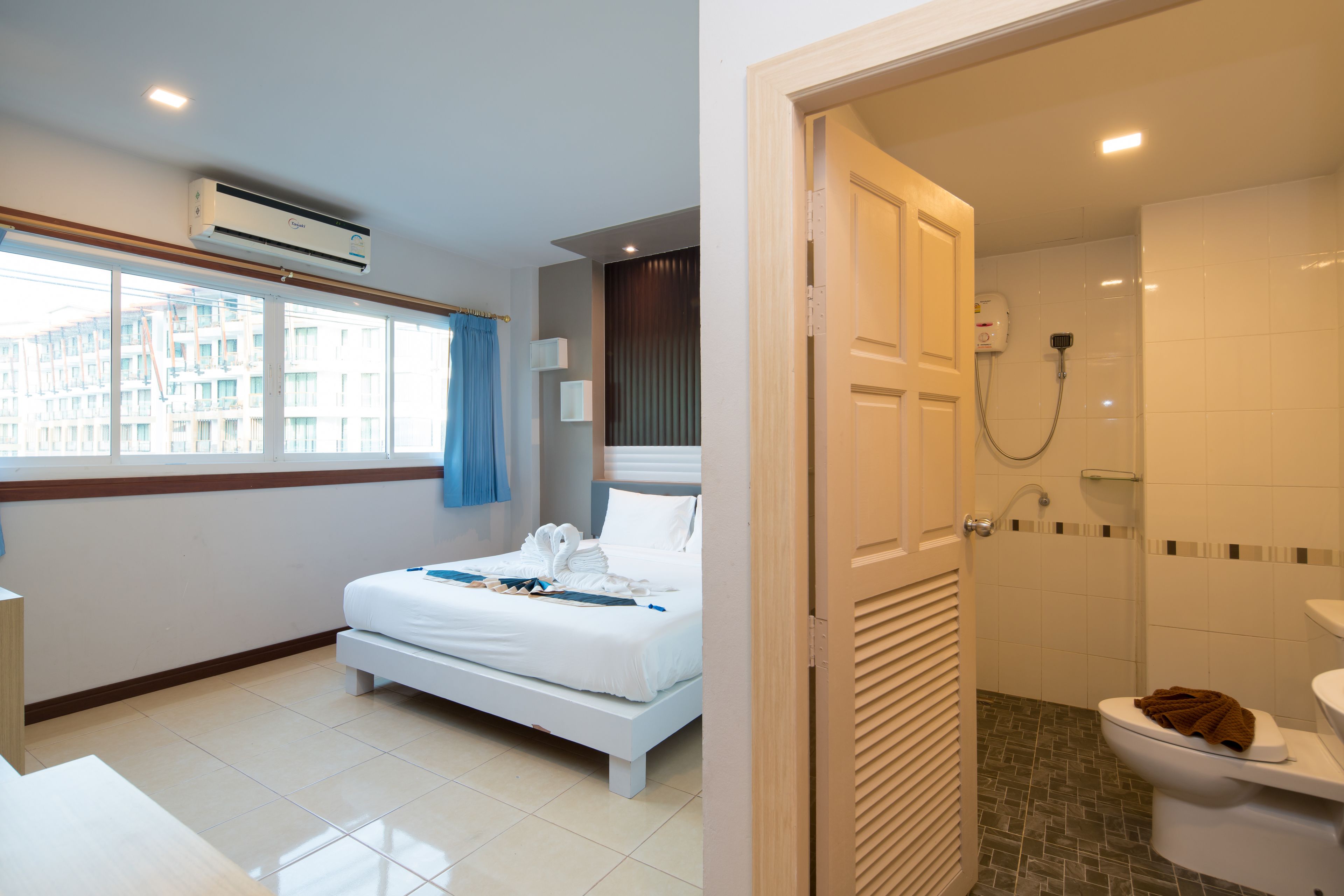Ein Hotelzimmer mit Bett, einem Badezimmer mit Toilette und Dusche sowie einem Fenster mit Vorhängen.