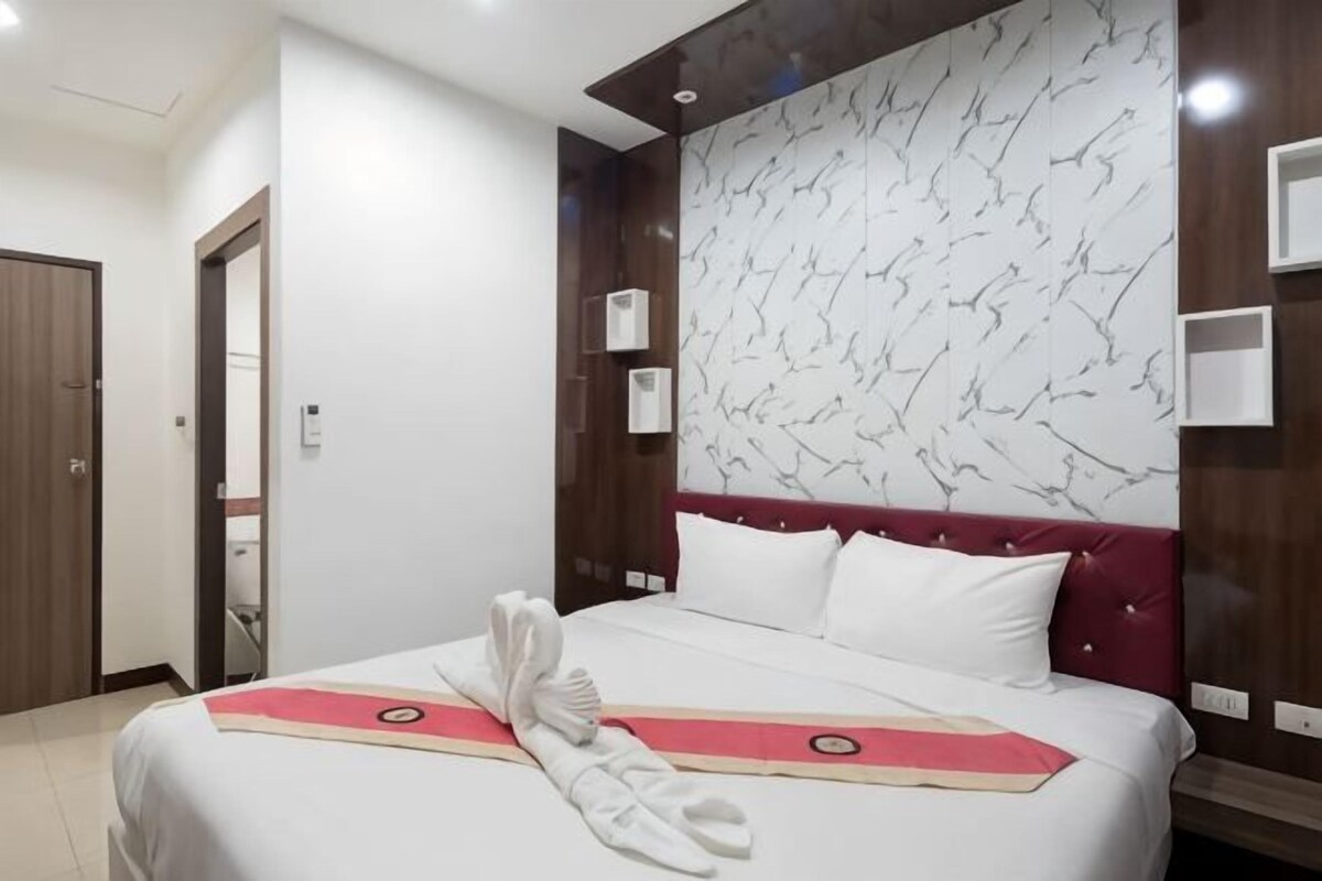 Habitación de hotel con una cama grande, cabecera roja, pared con diseño de mármol y puerta de madera.