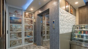 Um saguão de hotel com elevador de vidro, minibar e uma parede com padrões geométricos.