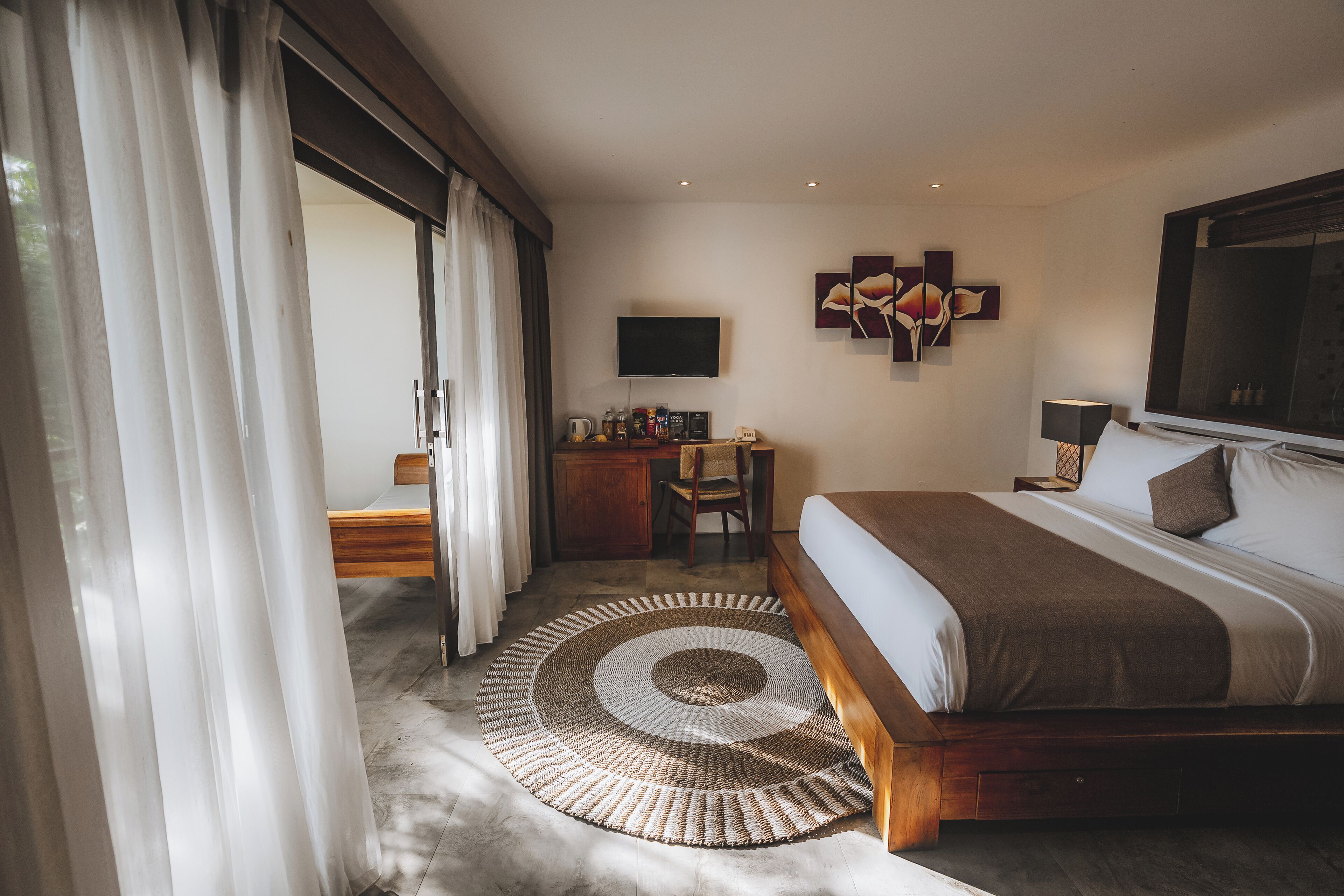Un dormitorio con cama, escritorio, silla, televisor y obras de arte en la pared.