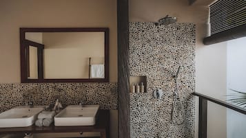 Une salle de bain avec deux lavabos, un miroir, une douche avec un mur en pierre et un porte-serviettes.