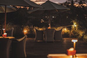 An outdoor dining area with wicker furniture and umbrellas, featuring a wooden deck and ambient lighting. - The Hidden Paradise Ubud (Ubud)