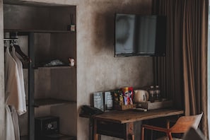 Une chambre d’hôtel équipée d’un bureau en bois, d’un téléviseur à écran plat, d’une armoire et d’une étagère contenant des articles de toilette.