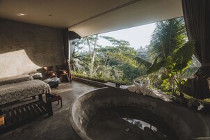 Una habitación con una bañera grande, un sofá y vistas a un paisaje tropical.