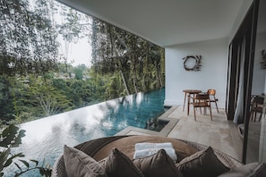 Un espace piscine extérieur moderne, avec vue sur une forêt luxuriante, comprenant un fauteuil de relaxation en osier et une petite table avec des chaises.