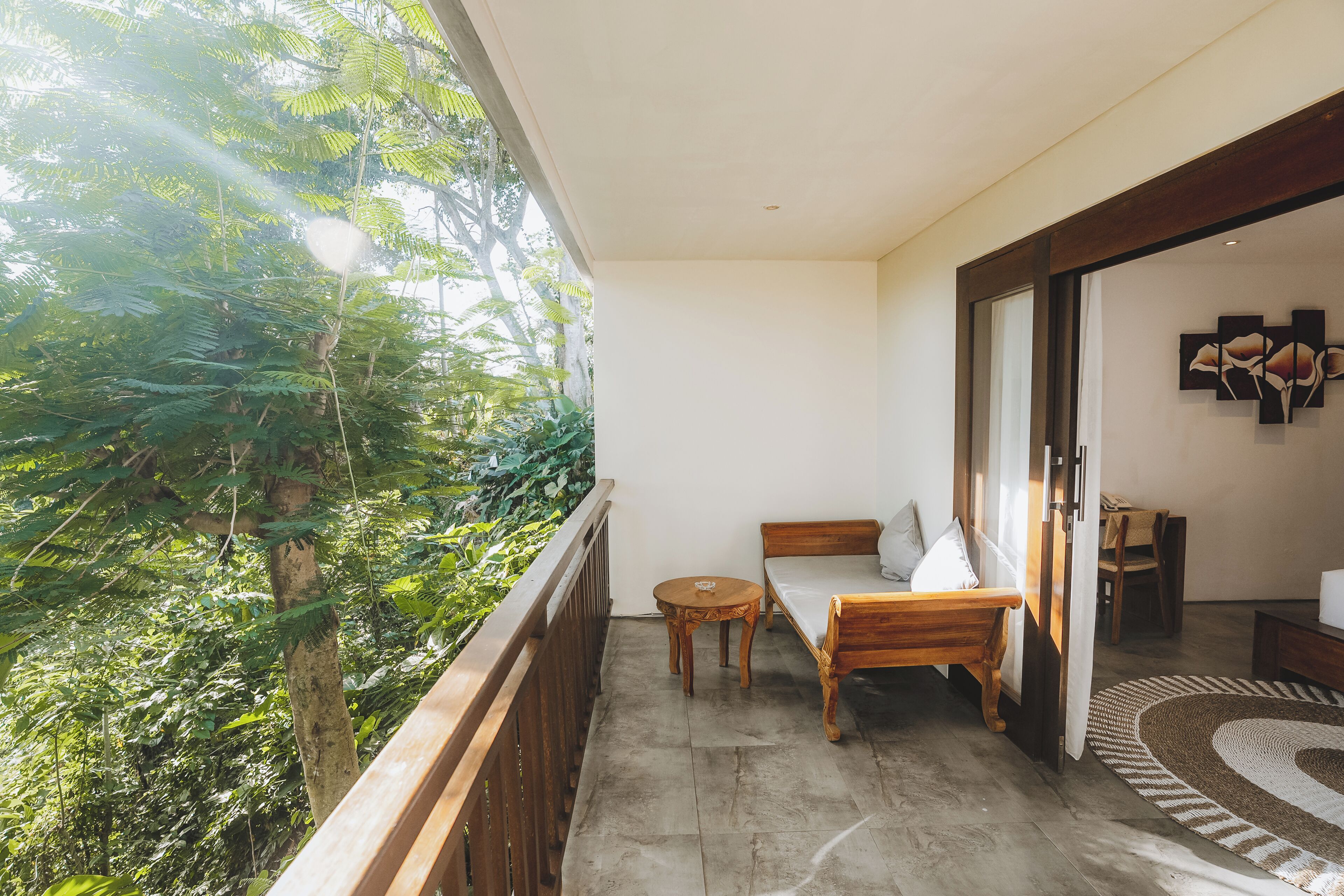 A balcony with a wooden table and a bed, overlooking a lush green area.
