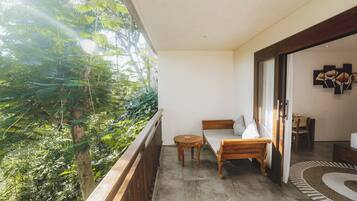 A balcony with a wooden table and a bed, overlooking a lush green area.