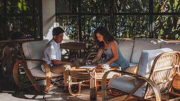A couple seated on a wicker sofa with a glass coffee table, surrounded by wicker chairs and a woven rug.