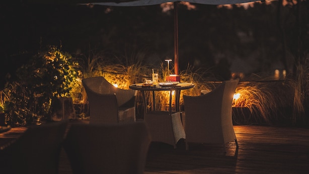 An outdoor dining area with wicker chairs and a table set for two, under a large umbrella.