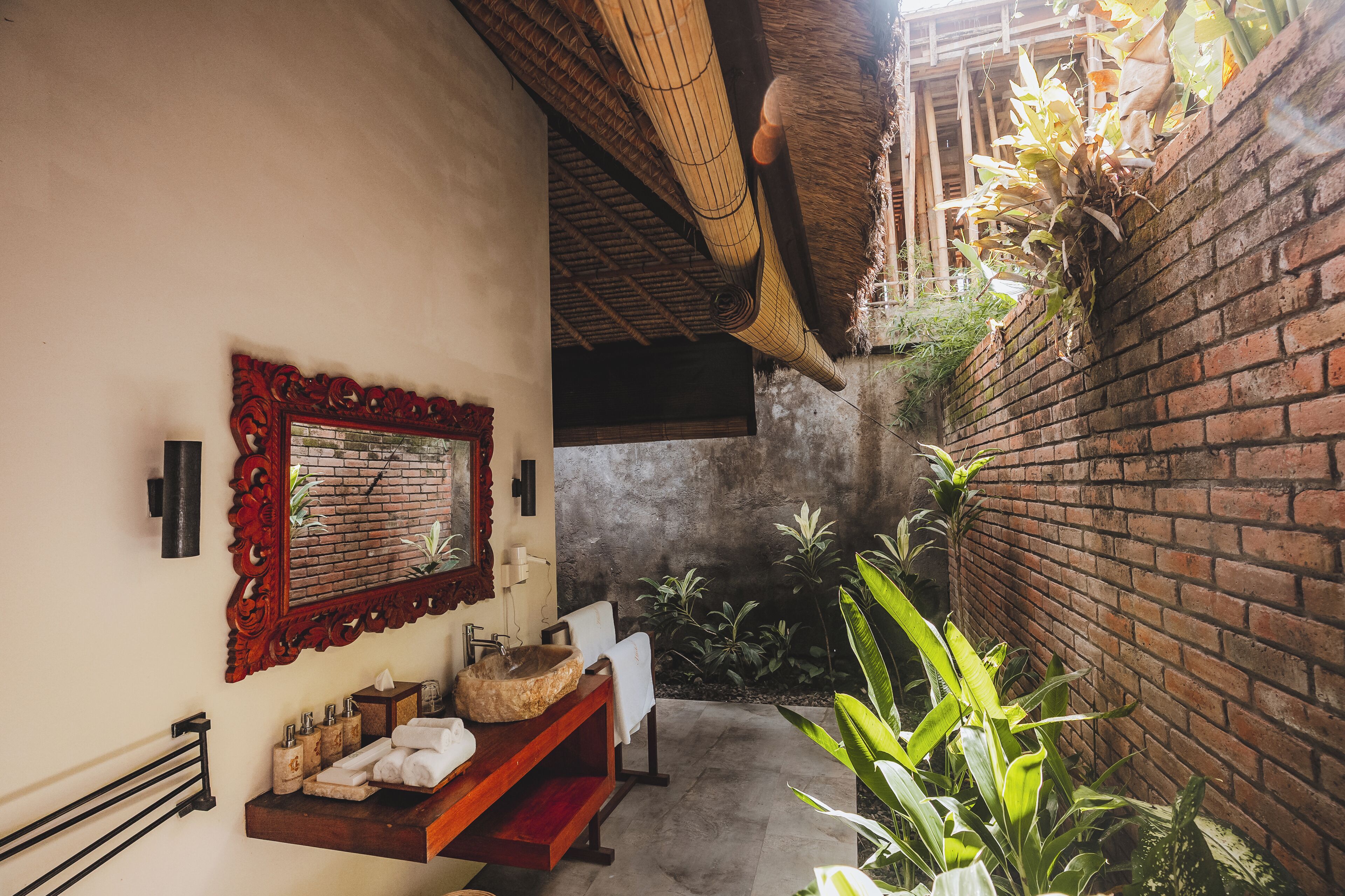 Un estrecho pasillo con pared de ladrillo, un banco de madera, un lavabo de piedra y un espejo con marco decorativo.