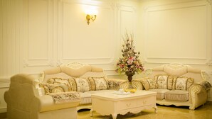 A luxurious living room with a cream-colored sofa set, a matching armchair, a white coffee table, and a floral centerpiece. - Hong Tung Hotel (Xuan Huong - Da Lat)