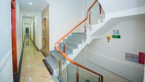 A hotel corridor with a glass railing staircase, a marble floor, and a sign indicating an exit. - Hong Tung Hotel (Xuan Huong - Da Lat)