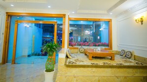 A spacious lobby with a seating area, a large potted plant, and a view of the outside through glass doors. - Hong Tung Hotel (Xuan Huong - Da Lat)