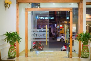 A hotel entrance with a glass door, potted plants, and a sign indicating the name. - Hong Tung Hotel (Xuan Huong - Da Lat)
