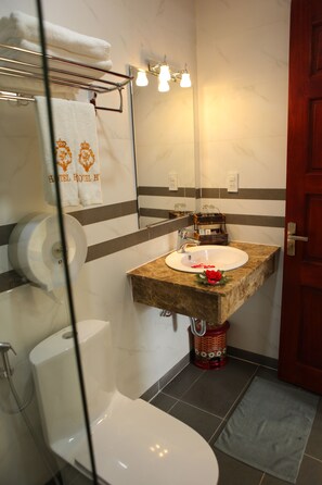 A bathroom with a white sink, a mirror, a towel rack with towels, a toilet, and a shower.