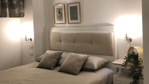A bedroom with a bed, two wall-mounted picture frames, a bedside table with a plant, and a nightstand with a lamp. - Edera e Camelie (Pompei)