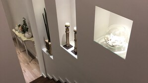 A staircase with dark wooden steps and white walls. There are three illuminated display cases on the wall, each containing different items. - Edera e Camelie (Pompei)