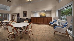 Un vaste espace dédié à la salle à manger, avec des tables rondes et des chaises en osier, un comptoir d’accueil en bois et de grandes fenêtres offrant une vue sur l’extérieur.